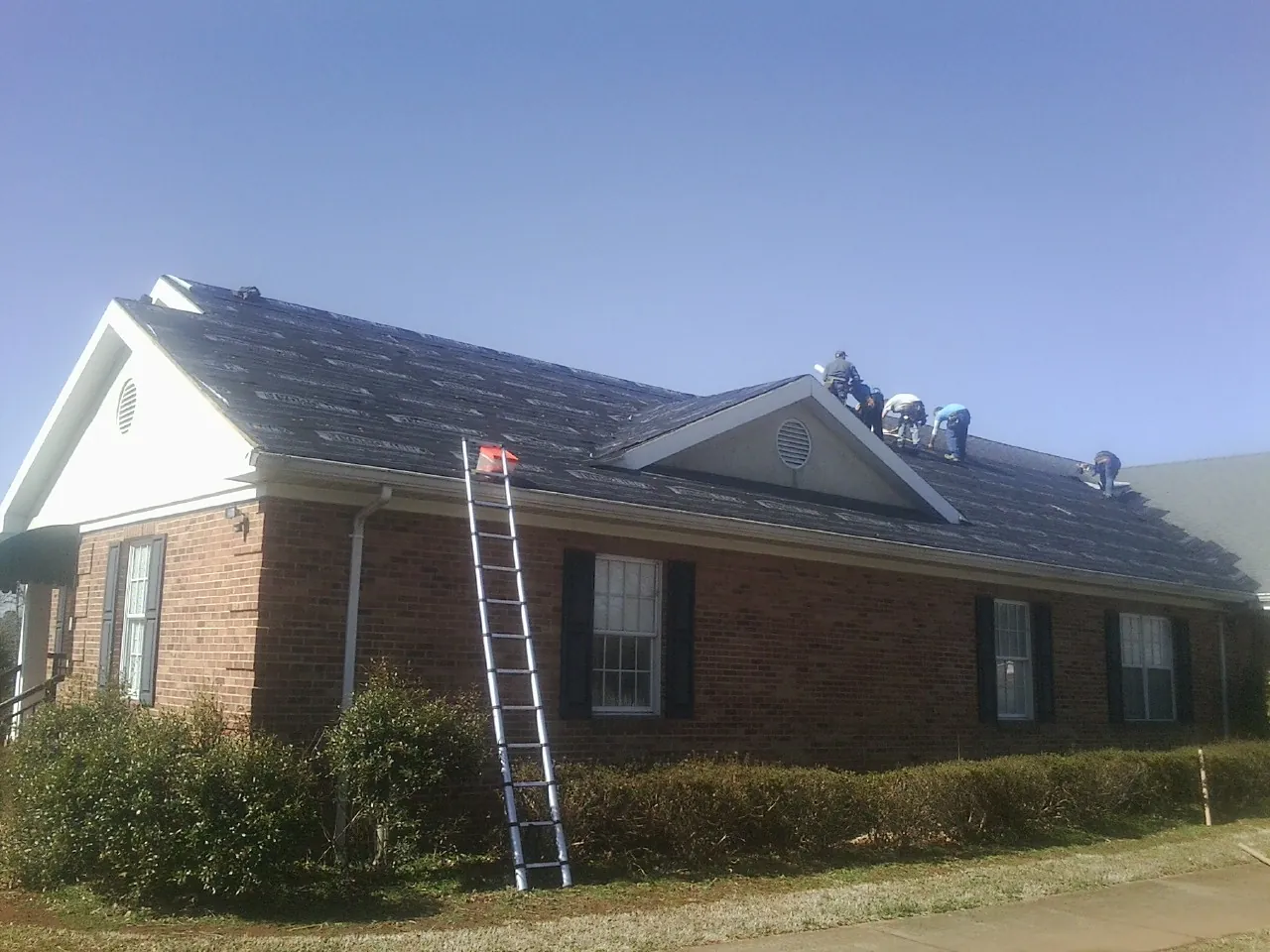 Crew tearing shingles off a brick ranch roof with a ladder set — Emergency Roof Repair work by our crew in North Branch