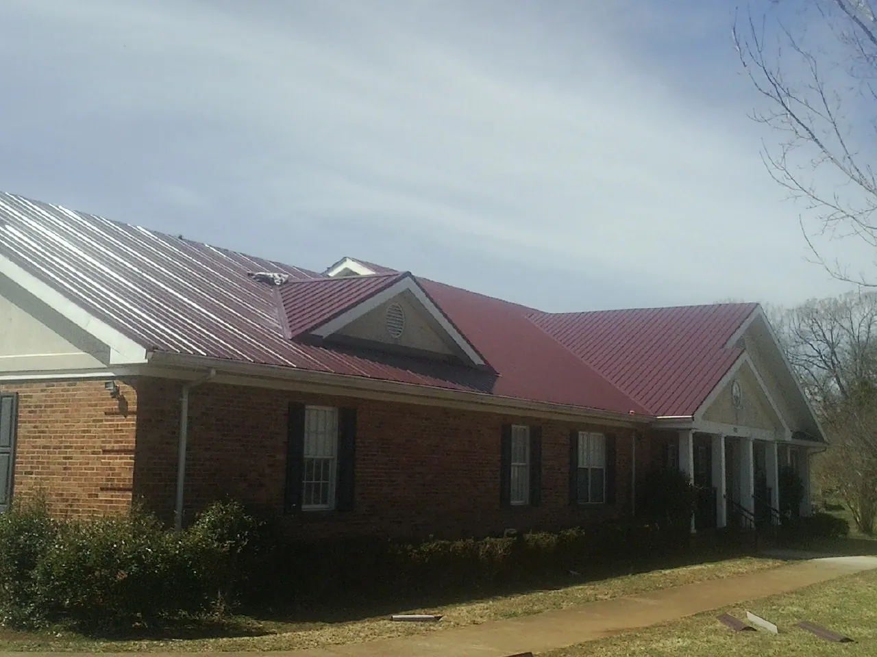 Red metal roof with gabled entries on a long brick building, from a Hail Damage Roof Repair job in North Branch