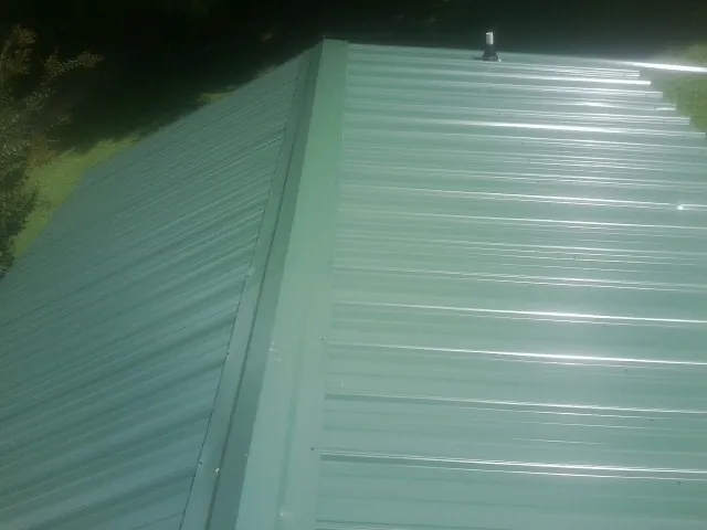 New green metal panels meeting at the ridge of a roof — Flat Roof Repair work by our crew in North Branch